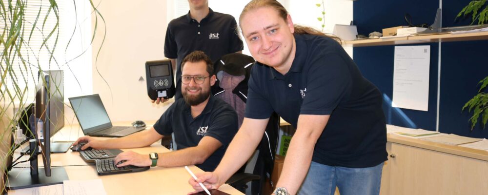 3 asut Mitarbeiter vor einem PC in einem Büro
